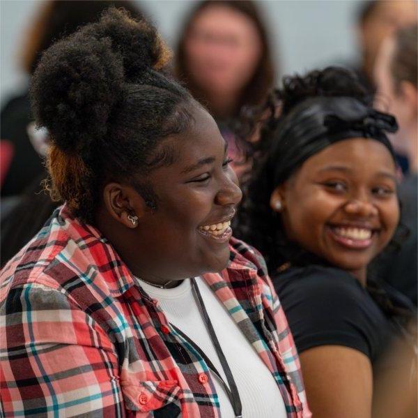 Two girls laugh as they listen to a speaker.